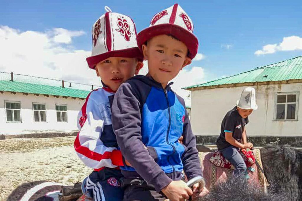 Kirgisische Kinder in Kalpaks im Pamir reiten auf Yaks